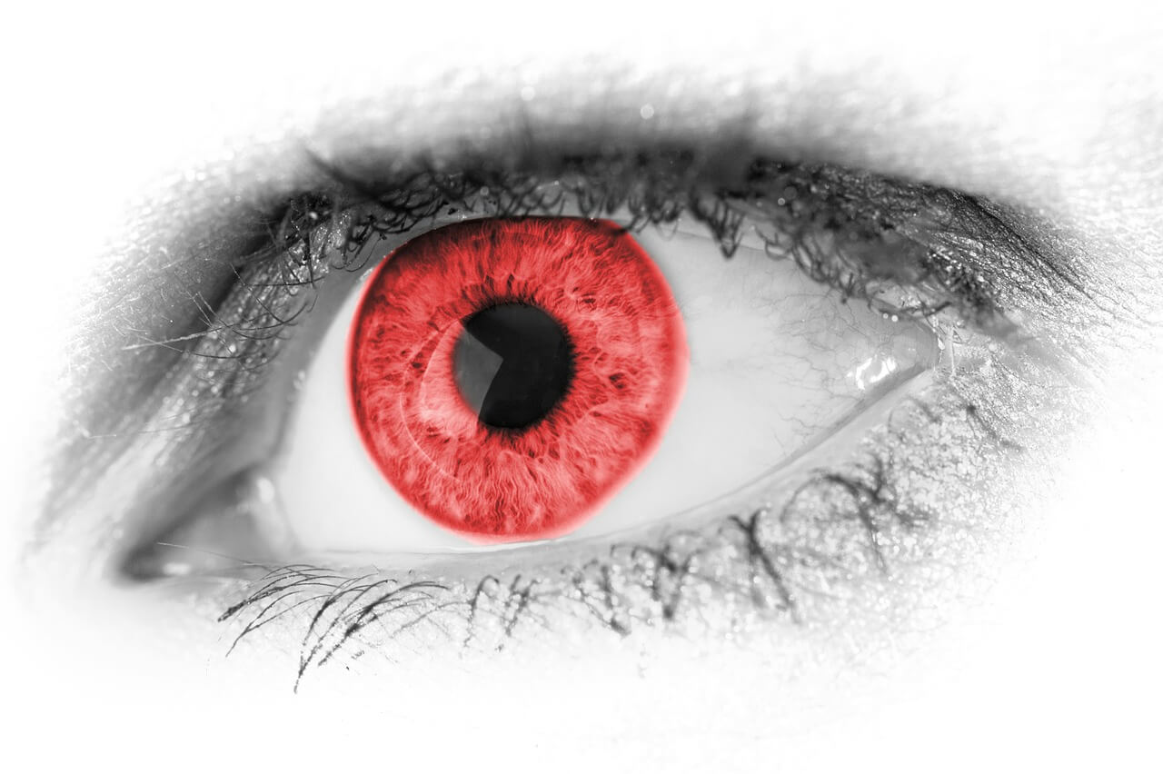 A close up of a greyscale eye with a red pupil.